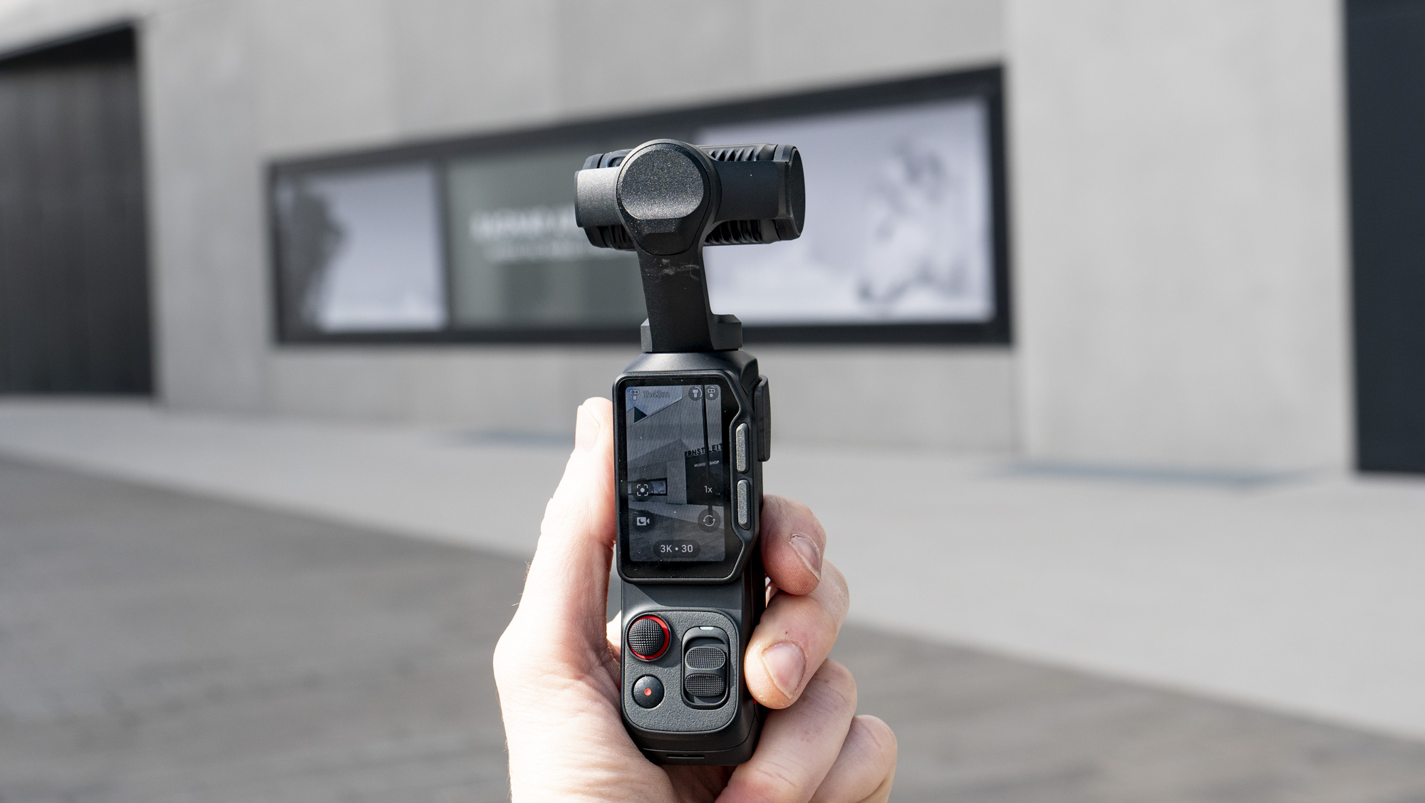 Insta360 Luna Ultra vlogging camera in hand, outdoors in gray urban scene