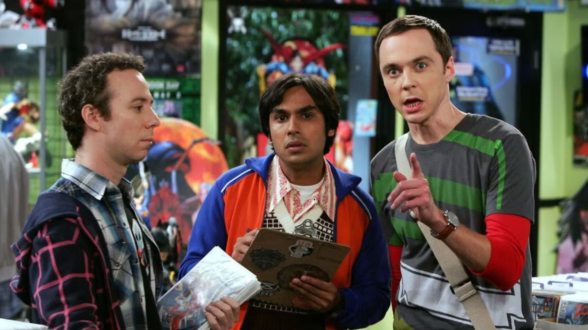 Sheldon points to something off-screen while Raj watches intently, while Stuart stares straight into space.