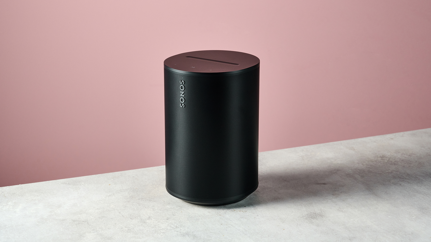 The Sonos Era 100 SL at a 3/4 sec angle in front of a pink background.
