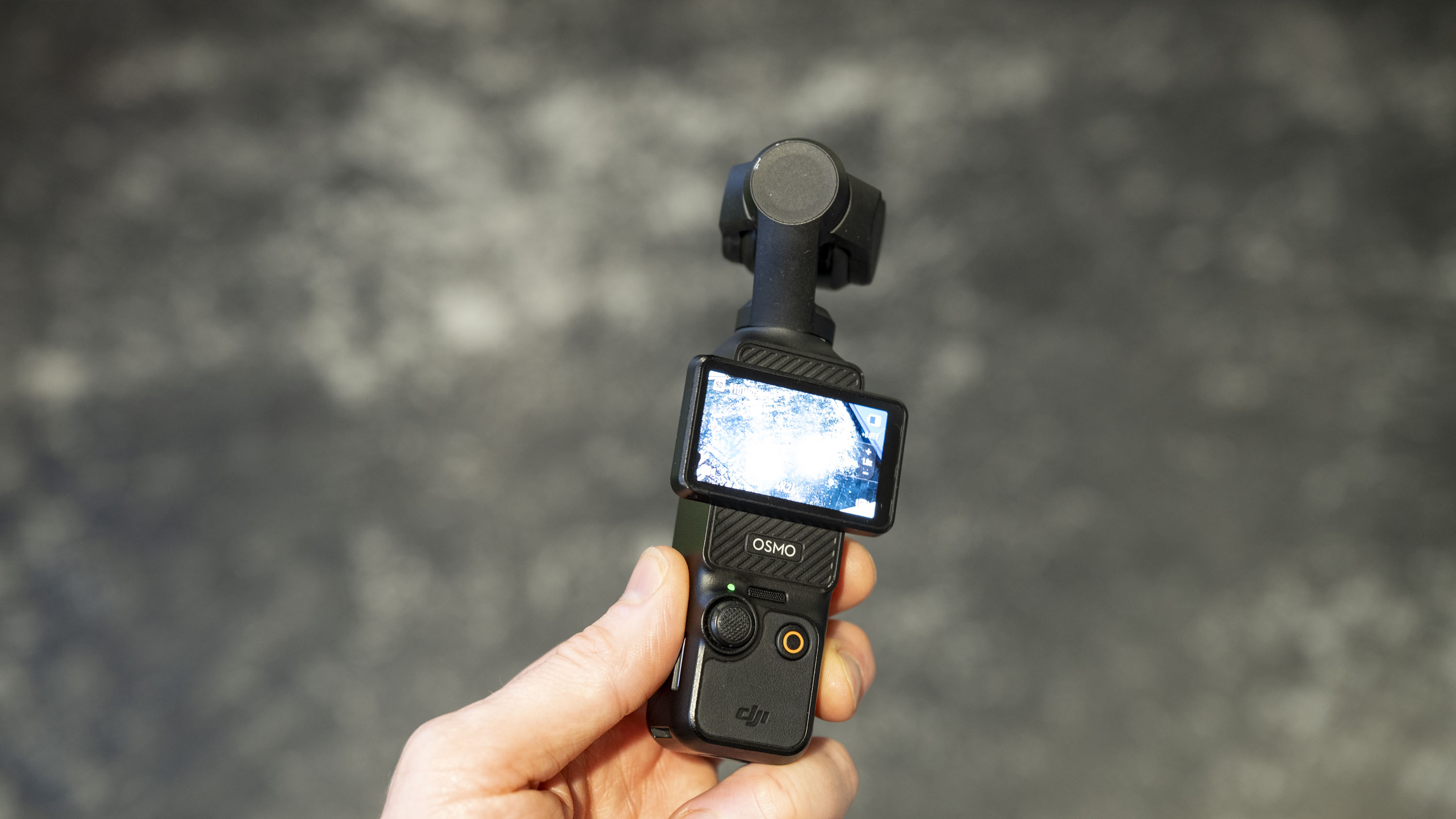 DJI Osmo Pocket 3 vlogging camera in user's hand, gray floor in background
