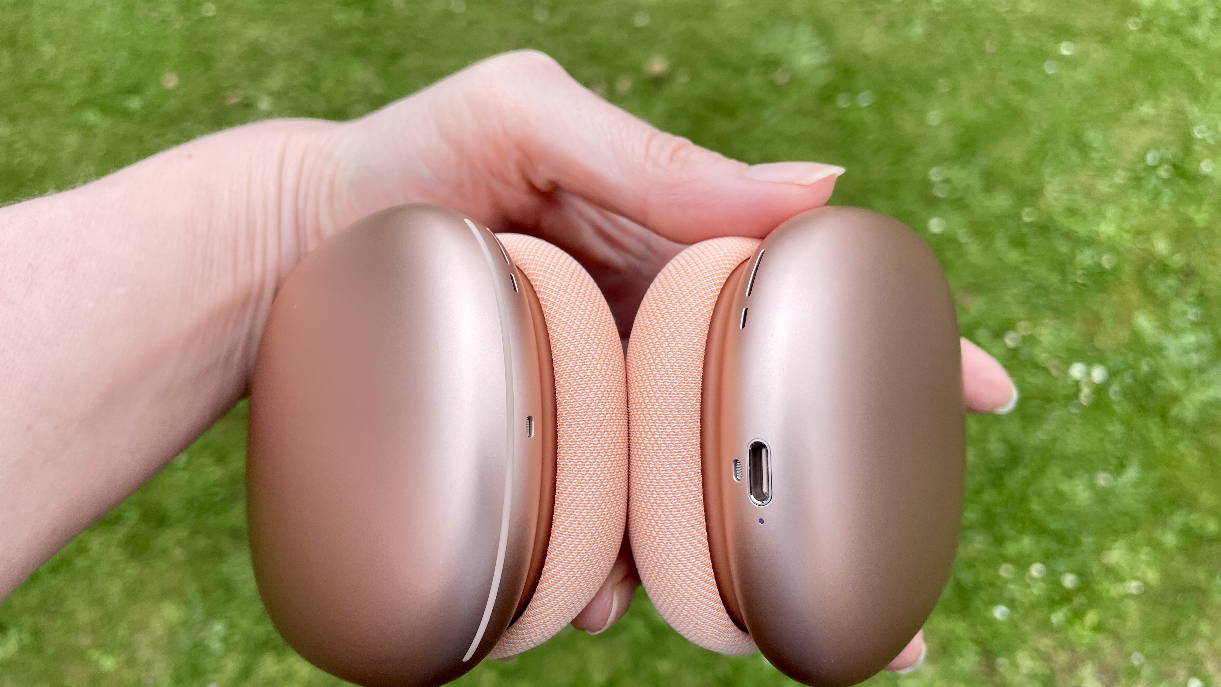 AirPods Max 2 in a garden, held in hand, close-up to show earbuds and strap