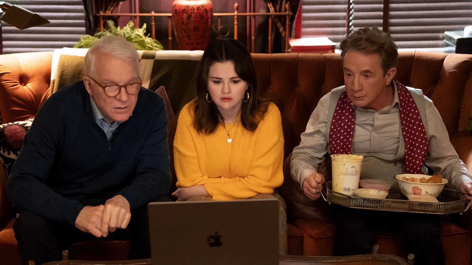 Steve Martin, Selena Gomez and Martin Short sit on a couch and look at a laptop, with a tray of food on Short's lap.