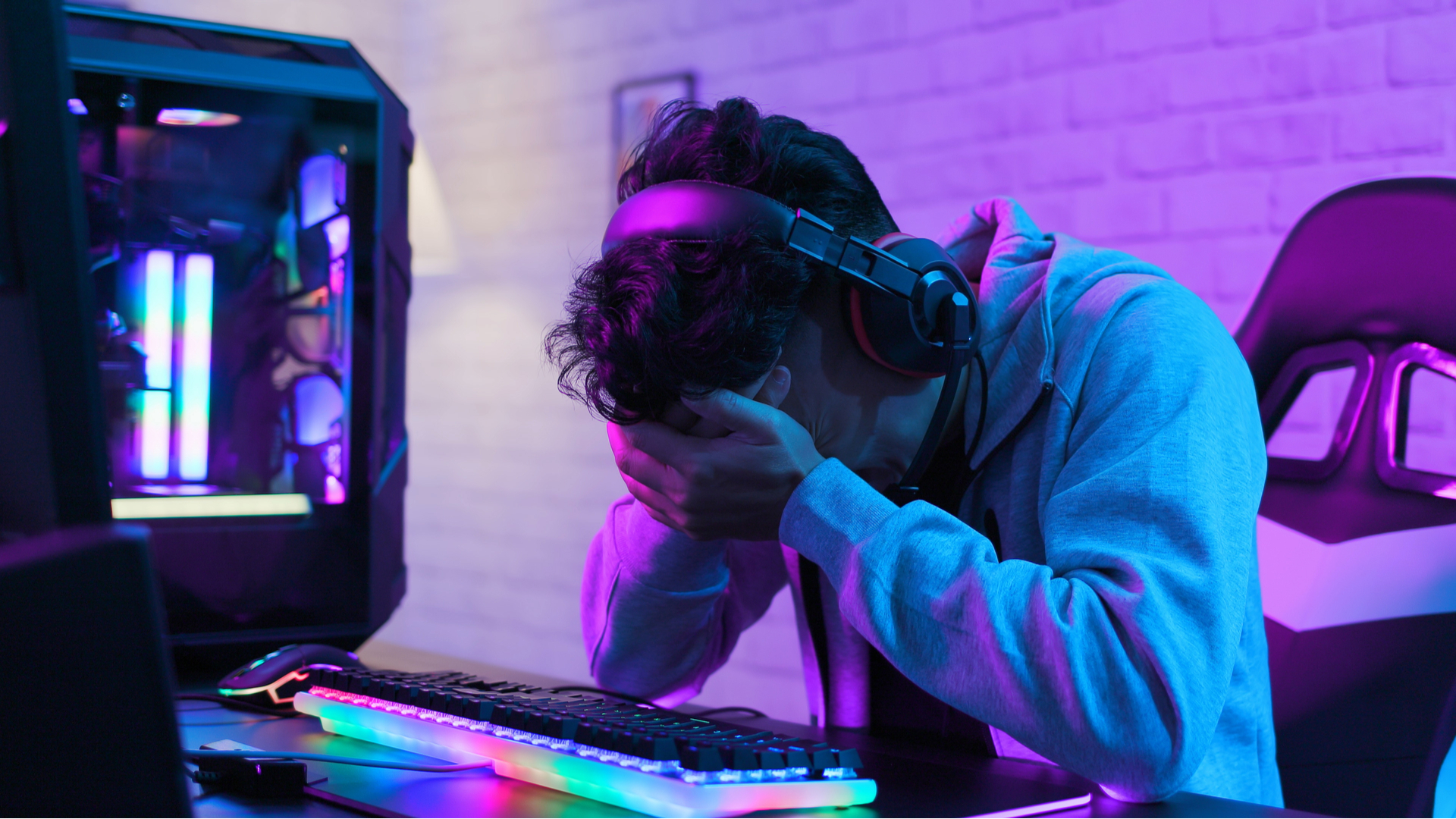 A sad person, holding his head in his hands, sat in front of a gaming PC