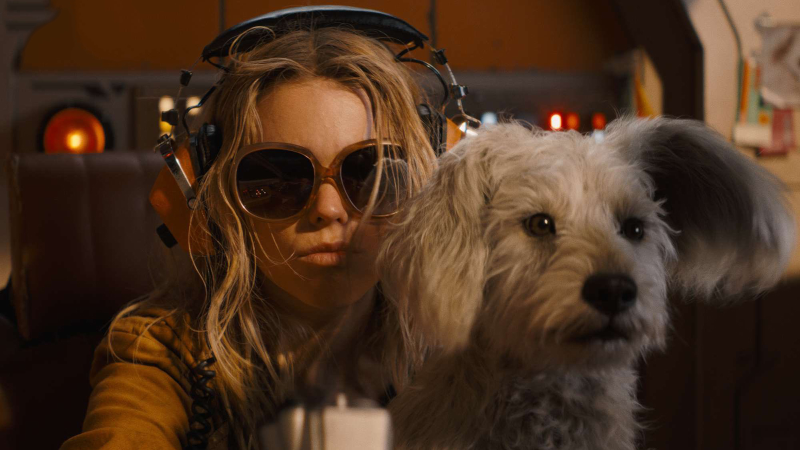 Kara wears sunglasses and headphones while sitting in a cockpit with Krypto on her lap in Supergirl