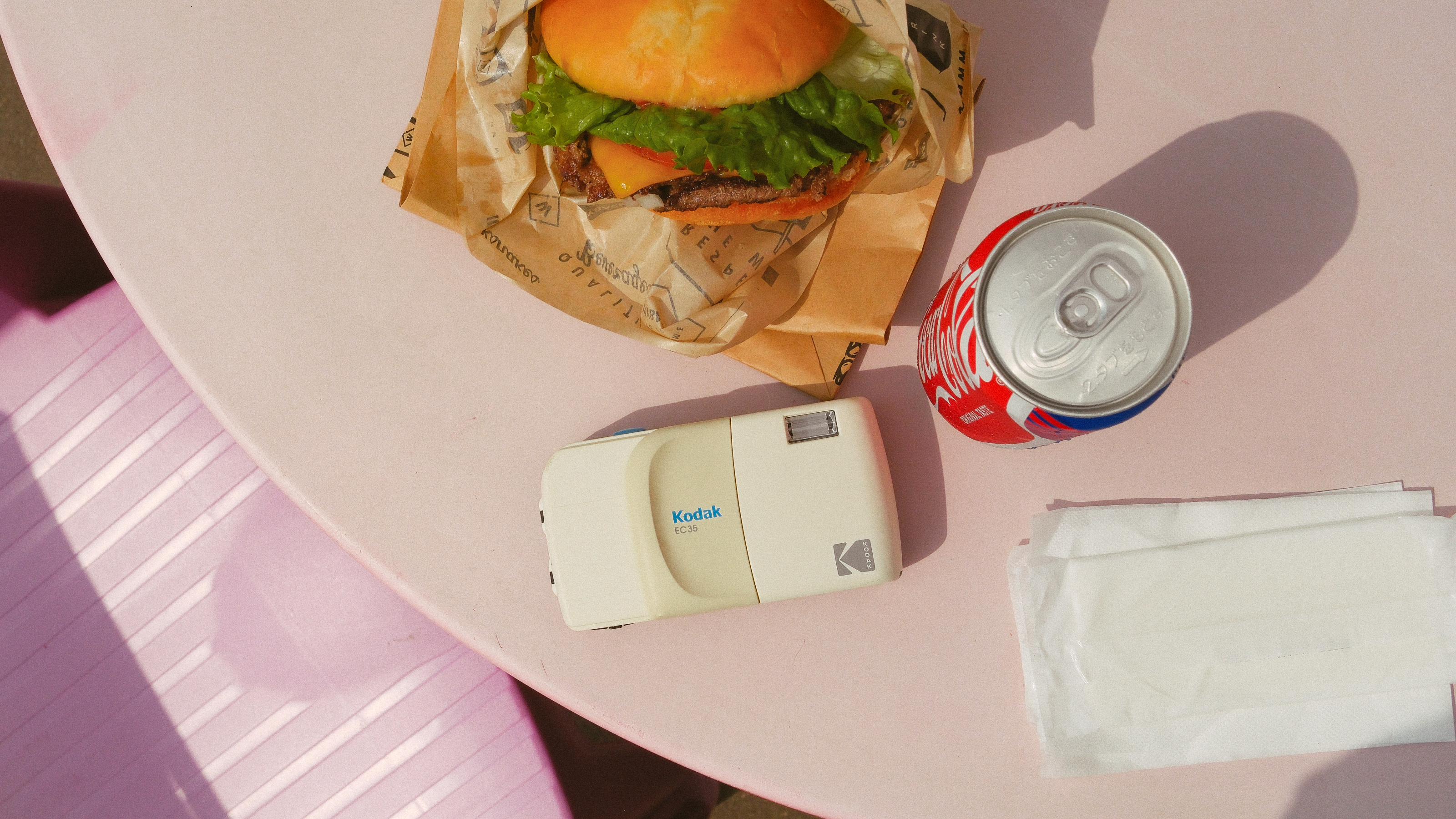 Photograph of Kodak EC35 film camera in white on a table next to a hamburger and a can of Coca-Cola