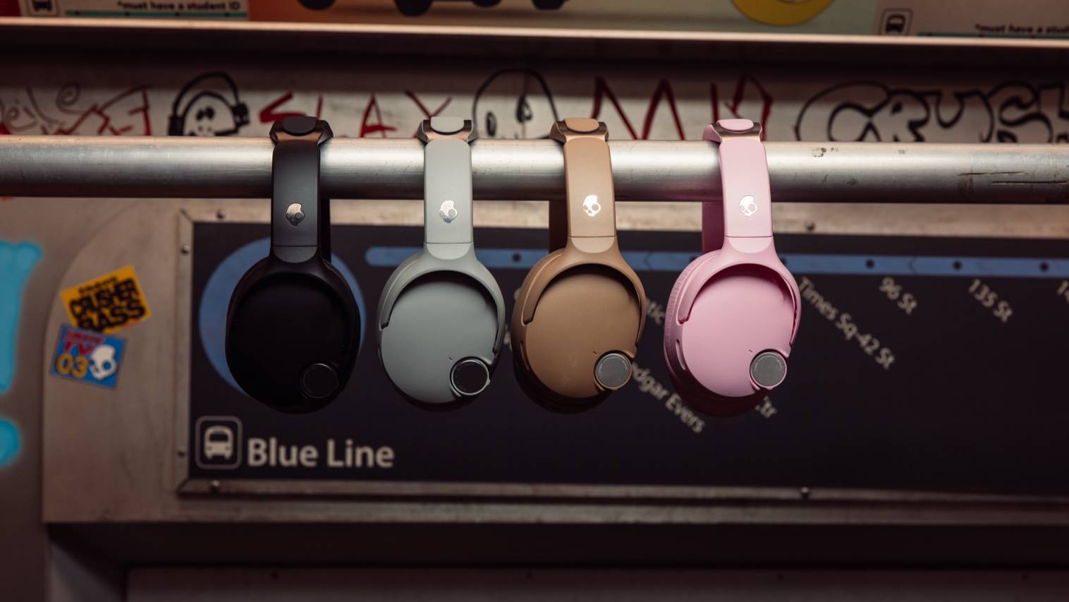 Four different colored models of Skullcandy Crusher 1080, hanging from a bar in a subway.
