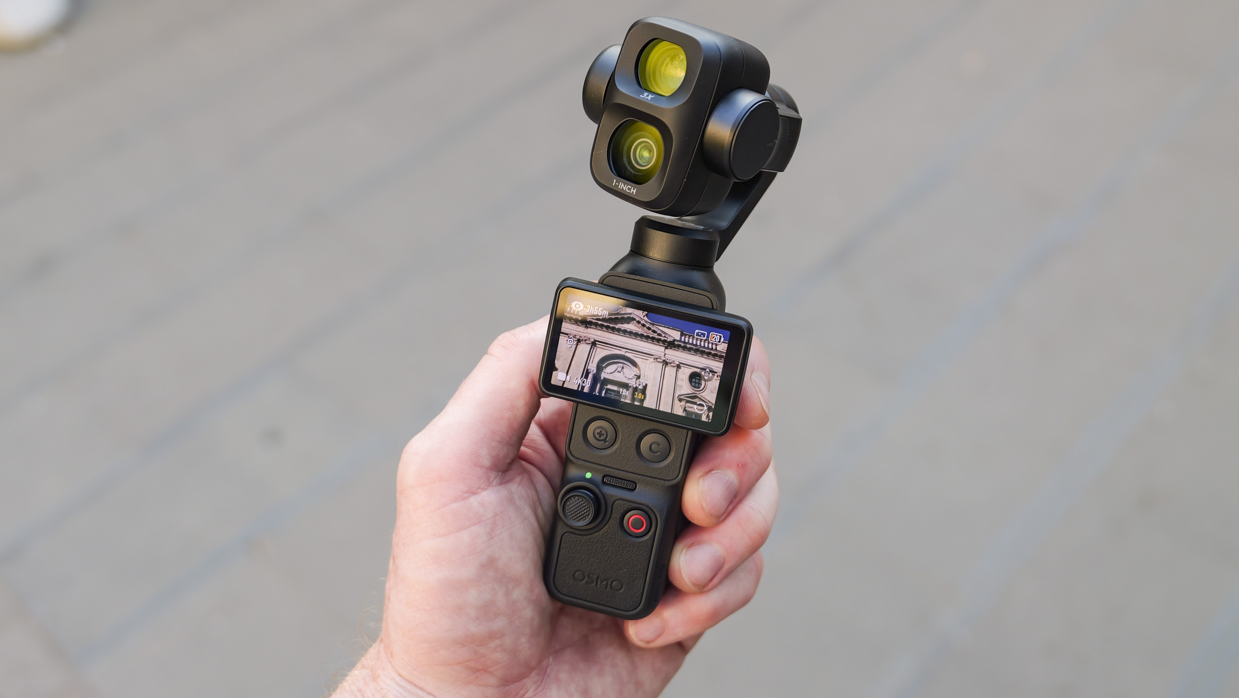 DJI Osmo Pocket 4P vlogging camera in a person's hand on a city street, screen shot horizontally